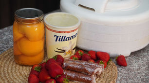 Jar of peaches, ice cream tub, strawberries, and wrapped treats on a woven mat. A white appliance in the background on a granite surface.