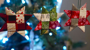 Three star-shaped fabric ornaments in red, green, and white hung on a Christmas tree with blue lights in the background.
