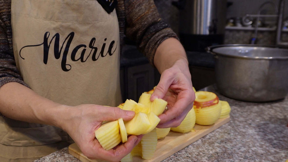 Person in an apron labeled "Marie" preparing sliced apples on a countertop. A large pot is in the background. Neutral kitchen setting.
