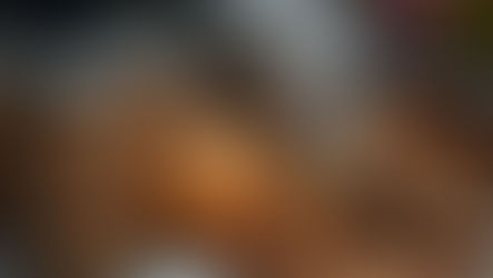 Jars of caramel, a ripe pear, and pecans spill from a wooden bowl on a speckled countertop in a kitchen setting.