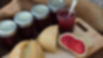 Jars of red jam labeled "superb" with a spoon in an open jar. Sliced bread with jam on a wooden board. Burlap background.