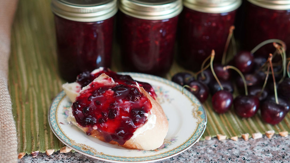 Plate with toast topped with cherry jam beside fresh cherries and jars of jam, on a green mat. Rustic and appetizing setting.