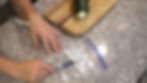 Hands labeling a plastic bag with "Zucchini 2024" using a marker on a speckled countertop; zucchini on a wooden cutting board nearby.