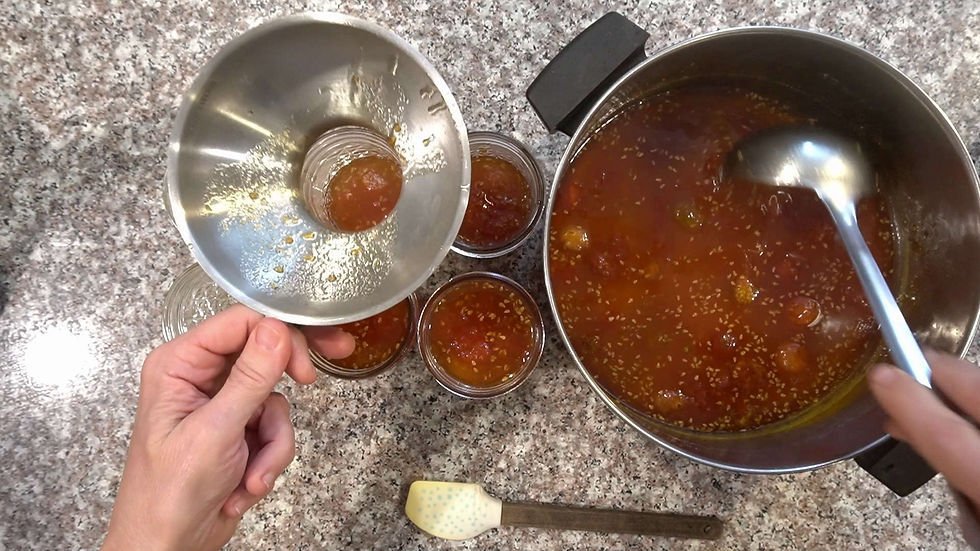 Hands fill jars with orange jam using a ladle and funnel on a speckled countertop, creating a cozy, homemade vibe.