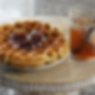 Waffle with syrup and nuts on a plate next to a jar of jam, set on a round wooden table. Warm colors and a cozy atmosphere.