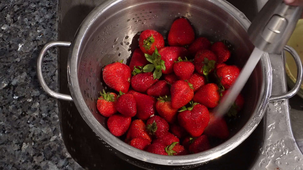Fresh strawberries in a metal colander being rinsed with water on a dark granite countertop, creating a clean and vibrant scene.