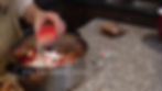 Person pouring lemon juice into a pot with strawberries and sugar on a granite countertop. Text: "1/4 cup Lemon Juice." Kitchen setting.