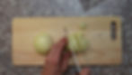 Hands slicing a yellow onion on a wooden cutting board atop a speckled countertop. The mood is focused. No text present.
