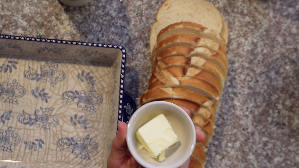 Sliced bread next to a patterned dish on a granite countertop. A hand holds a cup with a butter pat, suggesting a meal preparation.