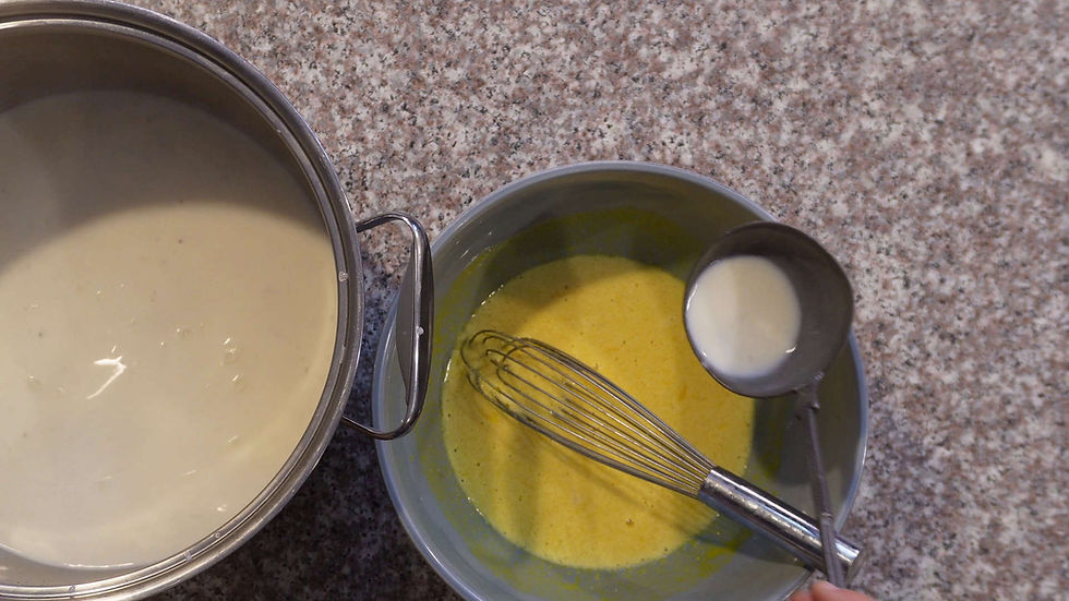 A ladle pours white liquid into a bowl with yellow mix and a whisk on a speckled countertop.