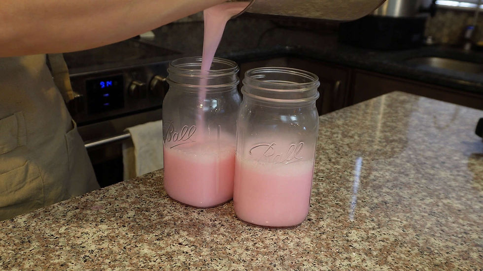 Pouring pink liquid into two mason jars labeled "Ball" on a granite countertop. Background shows a stove with the time 9:14.