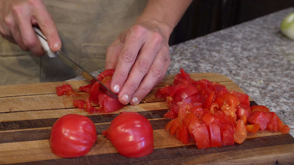 Hands slicing red tomatoes on a wooden cutting board in a kitchen. The setting is calm with a focus on the bright red color of the tomatoes.