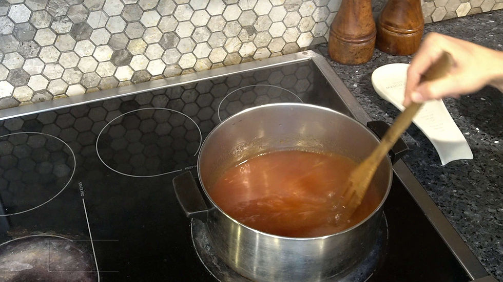 Hand stirring tomato sauce in a pot on a black stovetop, with a hexagonal tile backsplash and wooden shakers in the background.