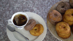 Tea in a floral cup with a bag, served with sugar-coated and plain donuts on a plate. Marble background, casual setting.