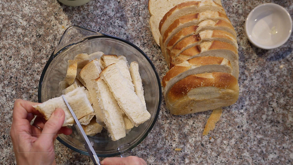 Hands slicing crust from bread into a glass bowl on a granite countertop. Sliced bread and an empty bowl are nearby.