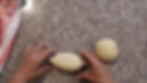Hands shaping dough on a speckled countertop beside a pink-striped cloth. Dough balls are evenly spaced, suggesting a baking preparation.
