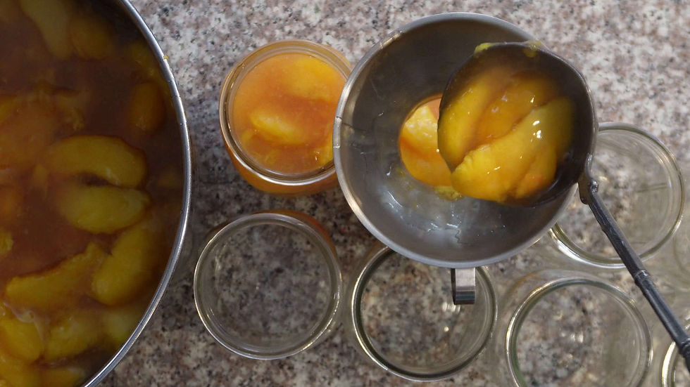 Jars being filled with sliced peaches in syrup using a ladle, set on a granite countertop. Bright orange peaches are visible in jars.