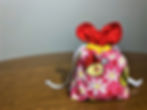 Colorful fabric gift bag with red ears and drawstrings, featuring ladybugs, daisies, and hearts on a pink background, placed on a wooden table.