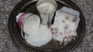 sugar scrub in cups sit on a tray: one tipped with coconut oil spilling, another upright, and one filled with lilac sugar.