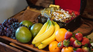 Fruit platter with bananas, oranges, strawberries, grapes and mangoes beside a candy tray labeled HARIBO on a wooden table