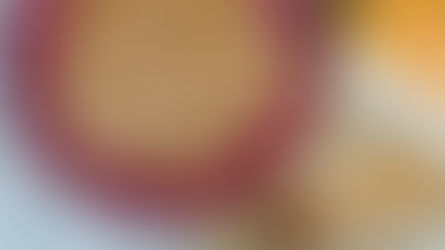 Red bowl of brown sugar on a woven placemat beside a loaf of bread and wooden spoon, viewed from above.