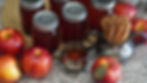 Jars of apple jelly, fresh red apples, and cinnamon sticks in a silver holder on a speckled countertop, creating a cozy, warm setting.