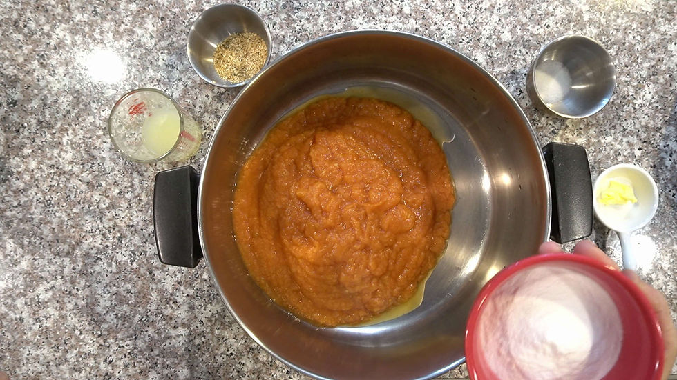 Bowl of orange puree on a granite counter surrounded by a measuring cup, spices, and butter. A red cup holds a white powder.