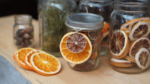 Jars filled with dried orange slices on a wooden surface. One jar is tied with a twine-held slice. Background includes more jars.