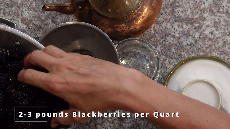 Hand placing blackberries in a bowl on a speckled countertop. Copper kettle and jars nearby. Text: "2-3 pounds Blackberries per Quart."