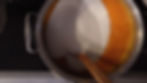 A pot with sugar and orange liquid is on a stove. A wooden spoon is partially submerged, stirring the mixture.