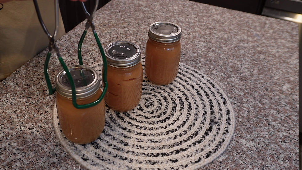 Three jars of brown liquid on a woven mat on a granite counter. One jar is being lifted with green metal tongs.