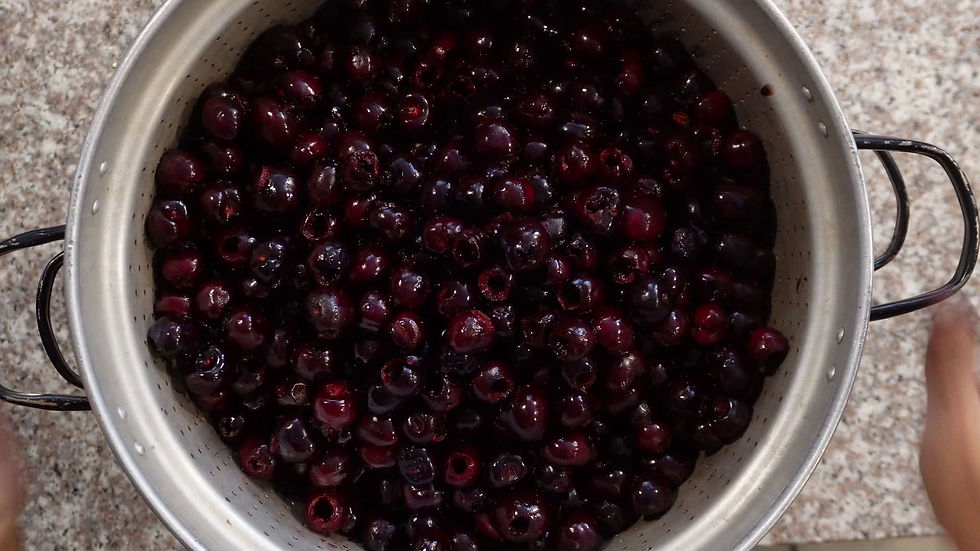 A large pot filled with dark purple cherries on a speckled countertop. Two handles are visible, suggesting it's being prepared or handled.