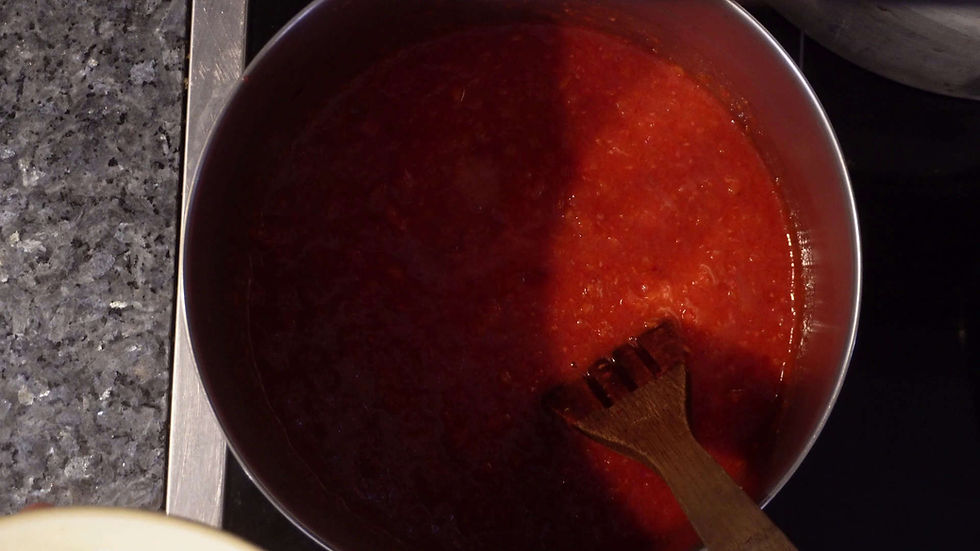 A pot of red tomato sauce being stirred with a wooden spoon. The setting is a kitchen with a dark granite countertop.