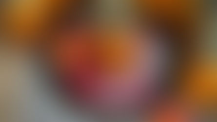 Jars of canned peaches on a red-checkered cloth with fresh nectarines and a decorative spoon on a silver tray, set on a woven mat.