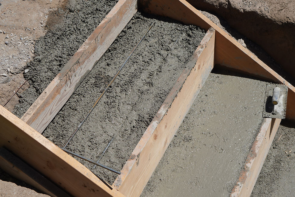 Wet concrete poured into wooden forms over rebar at a construction site, with rough dirt ground around it.