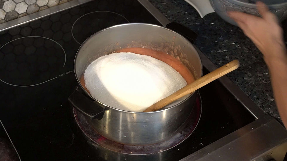 Pot on stove with sugar and pink mixture, wooden spoon inside. Marble countertop and hexagonal tile background. Hand reaching in.