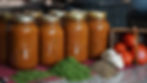 Jars of tomato sauce lined up on a counter with fresh tomatoes, garlic, and herbs. Cozy kitchen setting with warm, inviting colors.