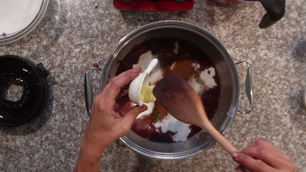 Hands adding butter to a pot of ingredients, stirred with a wooden spoon on a speckled counter.