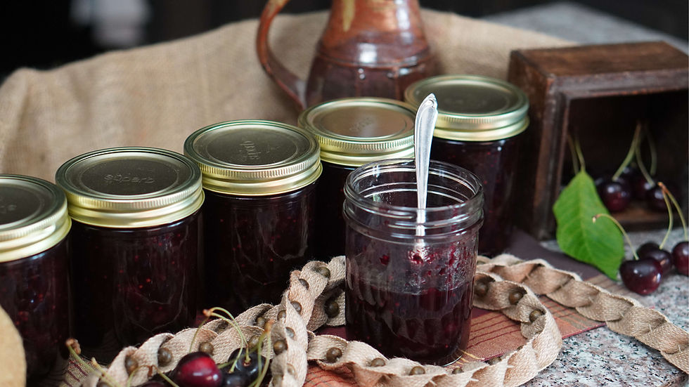 Jars of cherry jam on a rustic burlap backdrop. One jar is open with a spoon. Fresh cherries and a wooden box are nearby. Earthy tones.