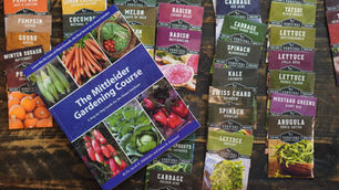 Gardening book with colorful seed packets for various vegetables on a wooden table. Text includes “The Mittleider Gardening Course.”