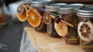 Jars filled with dried fruits and spices, including oranges and cinnamon, are arranged on a wooden surface. Earthy tones create a cozy vibe.