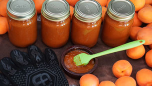 Jars of apricot BBQ sauce on a brown cloth, surrounded by apricots. A green brush in a bowl of sauce; text "superb" on jar lids.