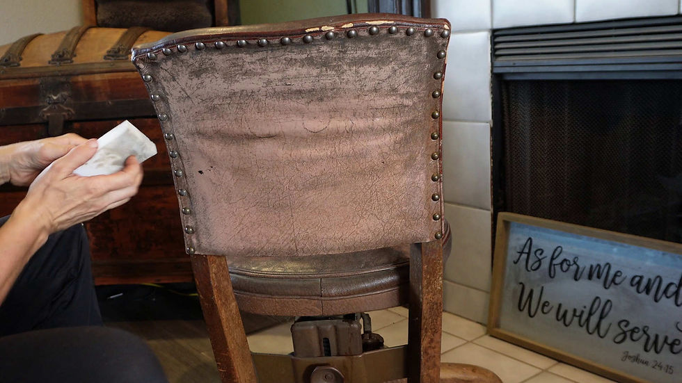 Hands cleaning a vintage chair with a cloth. Background shows a wooden chest and a sign reading "As for me and my... We will serve."