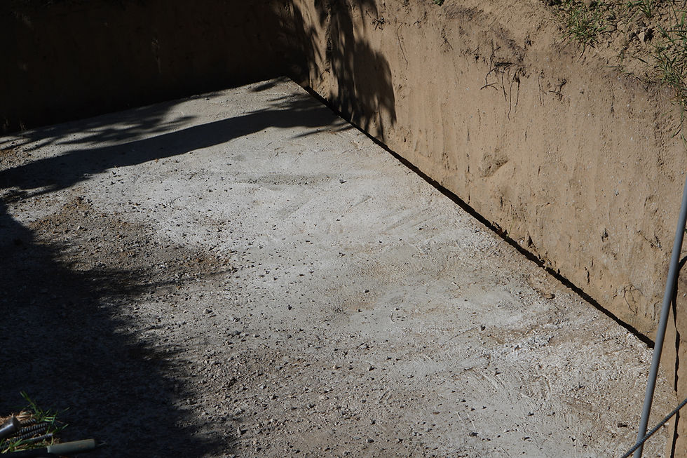 Concrete slab in a dirt trench, with strong shadows on tan earth walls and a quiet construction-site feel.