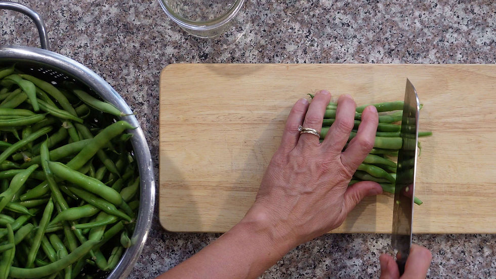 Hand slices green beans on a cutting board beside a bowl of beans in a kitchen, with a calm, focused prep scene.