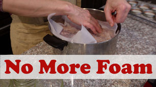 Hands arranging parchment in a pot on a speckled countertop. Nearby, empty glass jars; a person in a brown apron is partially visible.