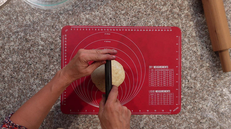 Hands shaping dough on a red silicone mat with measurement guides. Granite countertop and wooden rolling pin visible in the background.