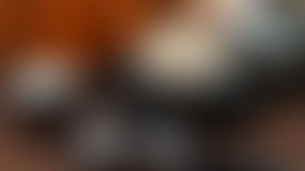 Ice cream in a glass bowl with a silver spoon, next to a metal jug of cream and an ice cream scoop on a brown surface. Warm background.