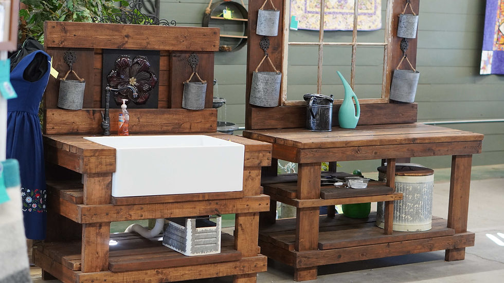 Rustic wooden sink displays with metal buckets, soap and watering can at an outdoor garden market, with a blue dress at left.