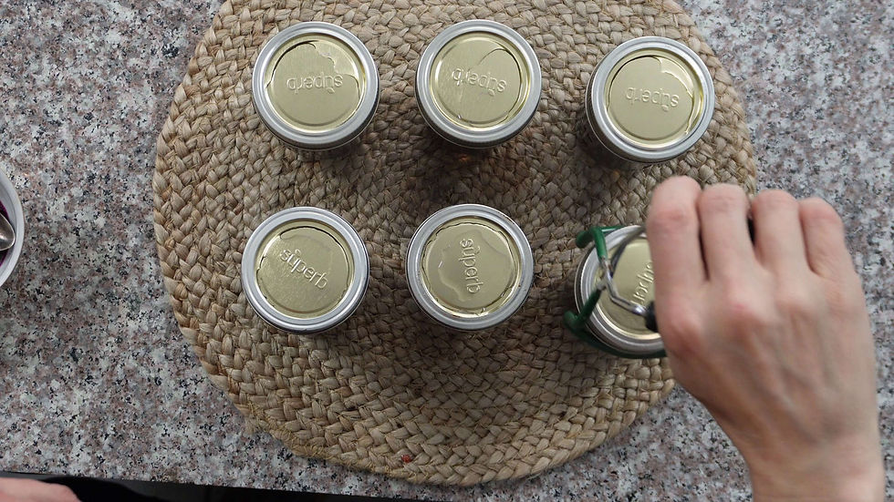 A hand using a jar lifter to pick up one of six sealed jars labeled "superb" on a woven mat, set on a speckled countertop.